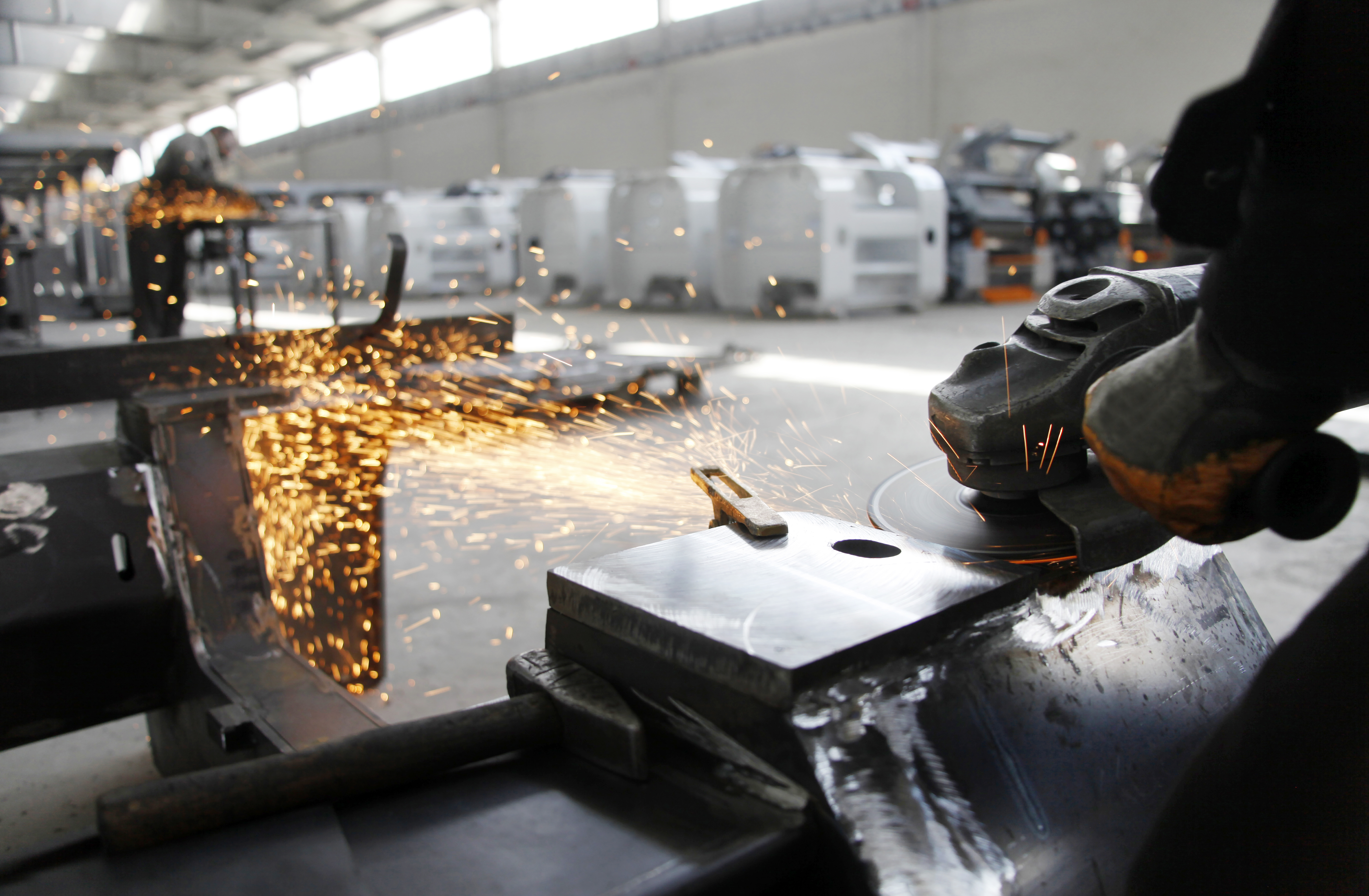 Metal fabrication worker cutting steel with sparks in modern factory