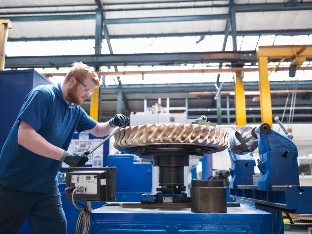 Engineer working on large bronze gear wheel in smart factory to improve manufacturing efficiency and capacity utilization